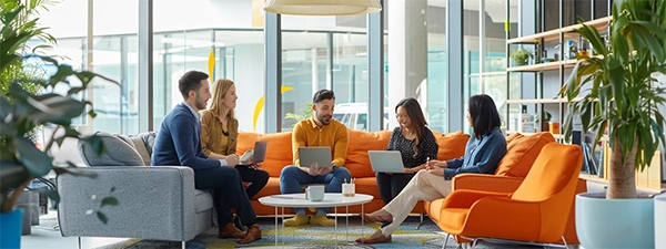  Several people relax on bright orange couches within an office, fostering a collaborative and inviting atmosphere.