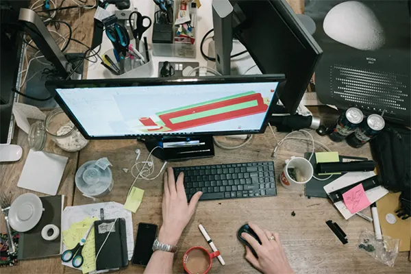 Top view of a messy workspace with a computer, notes, and scattered items on a desk
